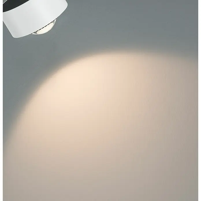 Paulmann URail LED-Spot Aldan - Signalweiß, Kaltweiß, Ø x H: 9,9 x 17,9 cm - Nahaufnahme einer weißen, runden Deckenleuchte, die ein warmes Licht auf eine graue Wand wirft. Elegant und funktional für moderne Räume.