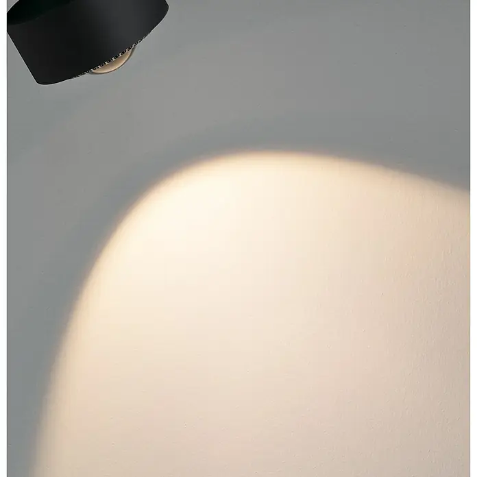 Paulmann URail LED-Spot Aldan - Schwarz matt, Kaltweiß, Ø x H: 9,9 x 17,9 cm - Nahaufnahme einer eleganten, schwarzen Lampe, die ein warmes, gerichtetes Licht auf eine helle Wand wirft und für Atmosphäre sorgt.