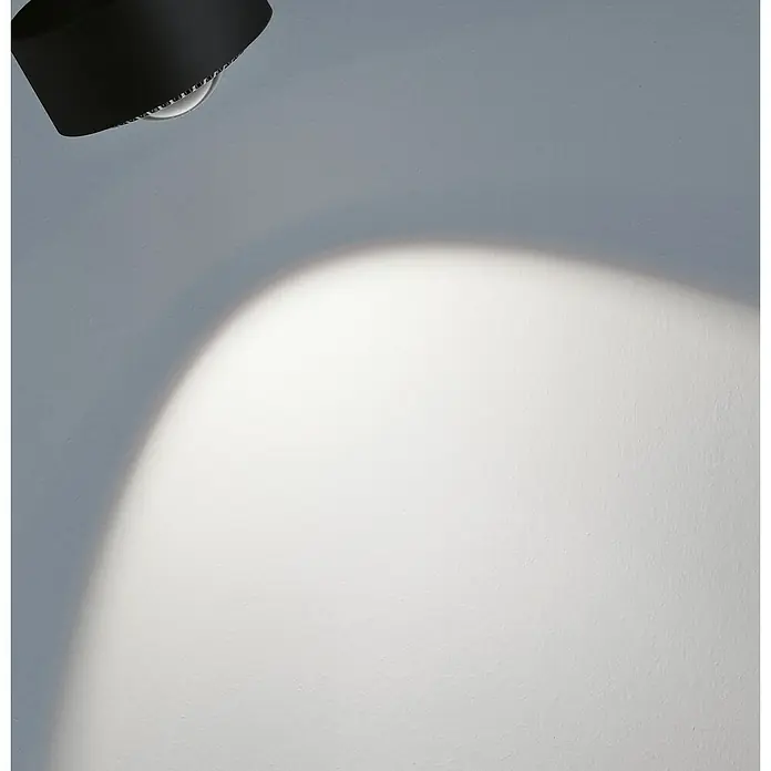 Paulmann URail Foco LED para riel Aldan - Negro, Blanco neutro, Ø x Al: 9,8 x 17 cm - Primer plano de una lámpara negra que proyecta un punto de luz brillante sobre una pared blanca.