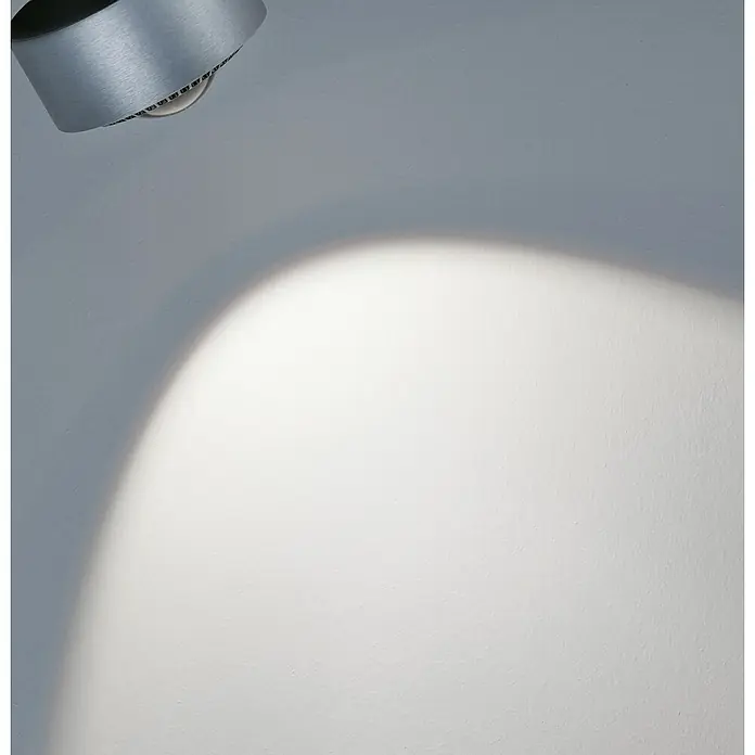 Paulmann URail LED-Spot Aldan - Chrom matt, Neutralweiß, Ø x H: 9,8 x 17 cm - Nahaufnahme einer modernen silbernen Lampe, die ein helles Licht auf eine weiße Wand wirft und eine minimalistische Ästhetik erzeugt.
