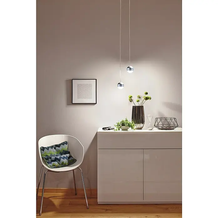 Paulmann URail LED-Pendelleuchte Capsule II - Neutralweiß, Chrom matt, Ø x H: 8,7 x 130 cm - Wohnzimmerinterieur mit einem stilvollen Schrank, einem Stuhl und zwei modernen Pendelleuchten, die für eine angenehme Atmosphäre sorgen.