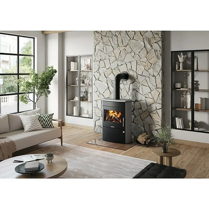 Justus Kaminofen Agero 2.0 - 7 kW, Raumheizvermögen: 144 m³, Material Verkleidung: Speckstein, Schwarz - Ein modernes Wohnzimmer mit einem Justus Kaminofen, der Wärme und Stil in den Raum bringt. Das Steinmauerwerk und die Regale ergänzen das elegante Design.