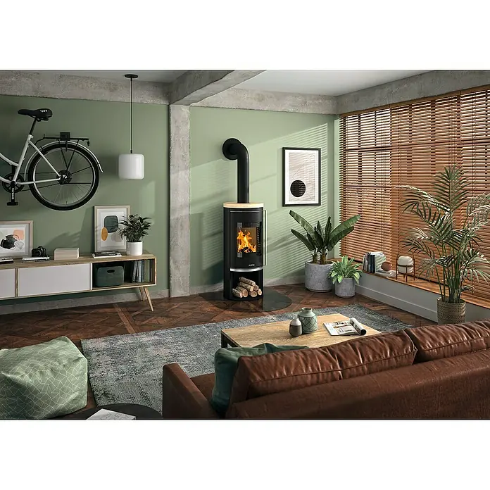Justus Kaminofen Faro 2.0 - 6 kW, Raumheizvermögen: 115 m³, Verkleidung: Stahl/Sandstein, Schwarz - Wohnzimmer mit einem Justa Kaminofen, braunem Ledersofa, Holzboden und einem an der Wand hängenden Fahrrad für eine gemütliche Atmosphäre.