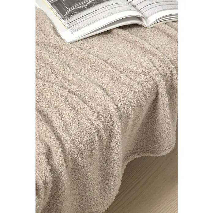 Manta para sofá Oslo - 160 x 220 cm, Poliéster, Beige - Primer plano de una manta de felpa beige con un libro abierto encima, ideal para sesiones de lectura acogedoras.