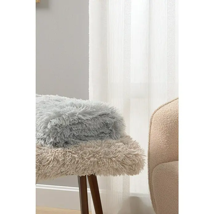 Manta para sofá New Luxury - 160 x 220 cm, Poliéster, Beige - Almohadas mullidas sobre un taburete de madera, ideal para un ambiente acogedor. Las texturas suaves invitan a la relajación y dan calidez.