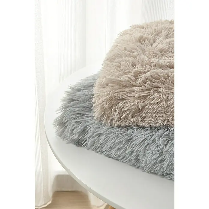 Manta para sofá New Luxury - 160 x 220 cm, Poliéster, Beige - Primer plano de dos cojines esponjosos en tonos beige y gris, apilados sobre una mesa blanca. Los cojines tienen una textura peluda.