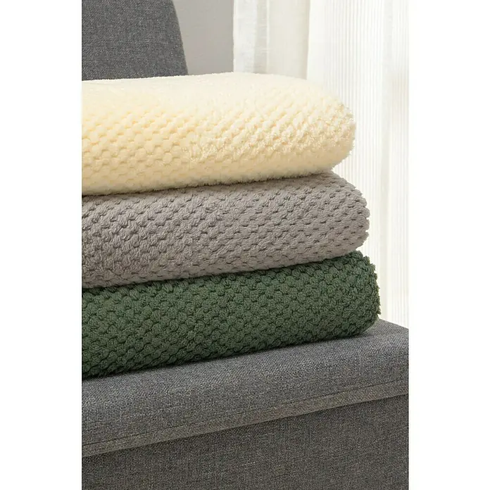 Manta para sofá Stelvio - 160 x 220 cm, Poliéster, Gris - Pila de tres mantas de felpa en crema, gris y verde oliva sobre un mueble gris, perfectas para añadir confort y estilo.