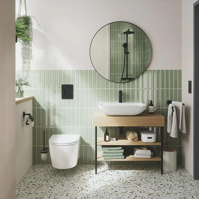 Grohe QuickFix Start Grifo de lavabo M - Profundidad del grifo: 121 mm, Negro, Mate - Baño con inodoro, lavabo con espacio de almacenamiento y espejo redondo. Azulejos verdes y suelo de terrazo añaden un toque moderno.