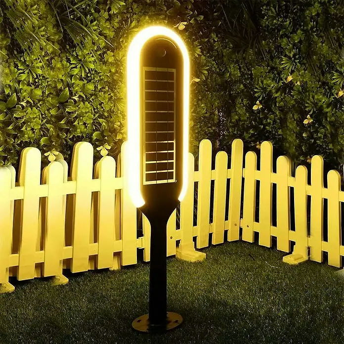Baliza exterior LED solar Denia - 3 W, Blanco neutro - Lámpara de jardín solar con borde LED y panel solar frente a una valla.