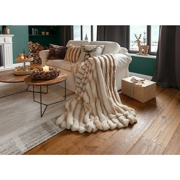 Kissen Hirsch - Braun, 45 x 45 cm, 100 % Polyester - Wohnzimmer mit kuscheliger Kunstfell-Decke in Beige- und Weißtönen über einem weißen Sofa drapiert, daneben ein Geschenk.