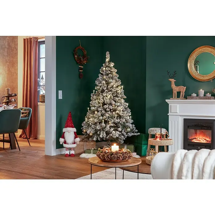 Künstlicher Weihnachtsbaum Imperial - Höhe: 180 cm, Grün, Standfuß - Ein festlich geschmücktes Wohnzimmer mit einem beleuchteten Weihnachtsbaum, einem Kamin und einem dekorativen Weihnachtswichtel.