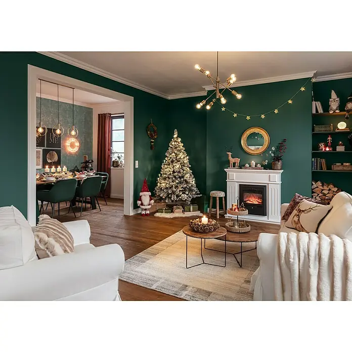 SCHÖNER WOHNEN-Farbe Wandfarbe DesignfarbeBesinnliches Waldgrün, Matt, 1 l, Konservierungsmittelfrei - Weihnachtlich geschmücktes Wohnzimmer mit einem beleuchteten Weihnachtsbaum, einem weißen Sofa und einem Kamin.