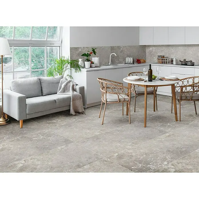 Feinsteinzeugfliese Tivoli Stone - 60 x 119,5 cm, Stärke: 7 mm, Smoke, Matt - Das Bild zeigt einen hellgrauen Fliesenboden in einem modern eingerichteten Raum mit Sofa, Esstisch und Küchenzeile. Die Fliesen haben eine elegante Marmoroptik.