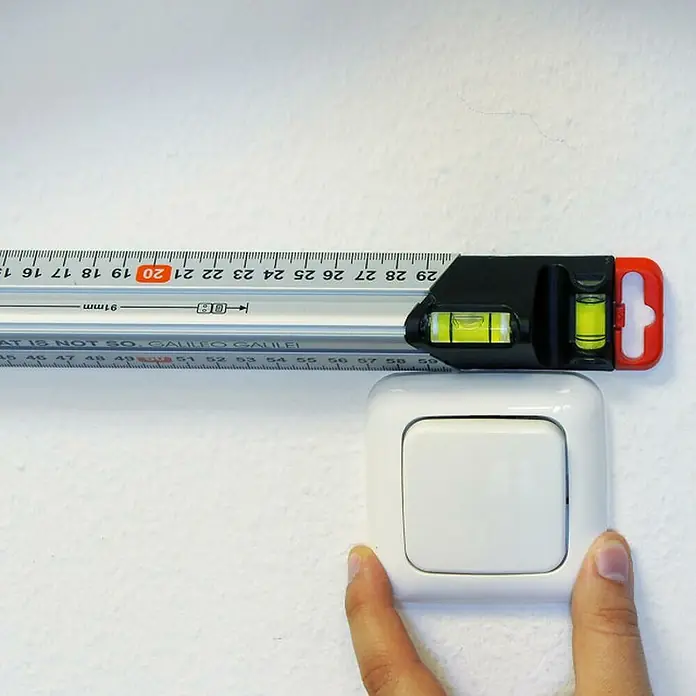 Connex Regla de marcado - Largo: 60 cm, Aluminio - Primer plano de un nivel de burbuja colocado sobre un interruptor de la luz, que indica si está nivelado.