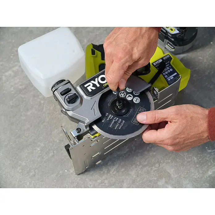 Ryobi Akku-Fliesenschneider RTS18C-0 - 18 V, Ohne Akku - Nahaufnahme einer RYOBI ONE+ Fliesensäge mit Händen, die die Klinge berühren, mit Fokus auf Details und Funktionalität des Werkzeugs.