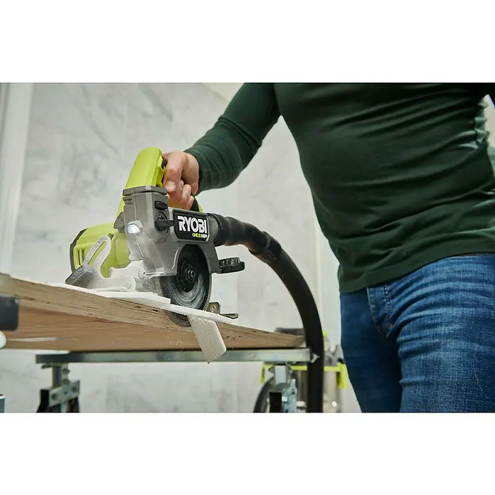 Ryobi Akku-Fliesenschneider RTS18C-0 - 18 V, Ohne Akku - Eine Ryobi ONE+ HP Kompakt-Kreissäge schneidet ein Holzbrett. Der Bediener ist mit Jeans und grünem Oberteil bekleidet.