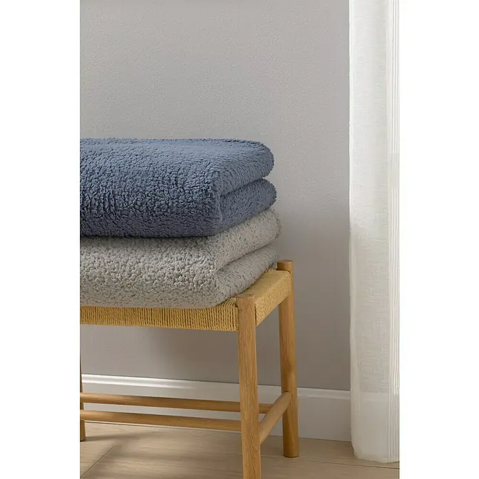 Manta para sofá Lucerna - 170 x 230 cm, Poliéster, Gris - Pila de mantas sherpa azules y grises sobre un taburete de madera, prometiendo confort y calidez para su hogar.