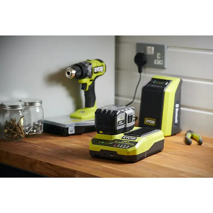 Ryobi ONE+ Akku-Schnellladegerät RC18180 - Passend für: Ryobi One+ 18V Akkus - Nahaufnahme eines Ryobi ONE+ 8A Schnellladegeräts mit einem Akku, einem Akku-Audioplayer und einem Ryobi-Bohrer im Hintergrund.