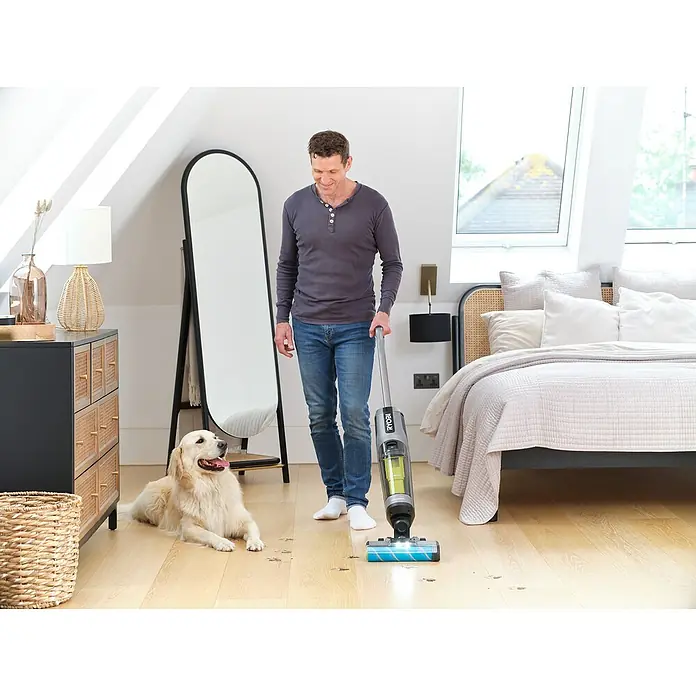 Ryobi ONE+ Akku-Hartbodenreiniger RHFC18BL-0 - 18 V, Ohne Akku, Luftmenge: 710 l/min - Mann saugt mit dem RYOBI Akku-Nass-Trockensauger den Boden, während ein Golden Retriever daneben liegt.