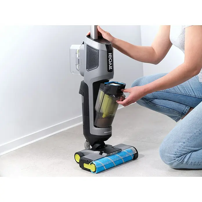 Ryobi ONE+ Akku-Hartbodenreiniger RHFC18BL-0 - 18 V, Ohne Akku, Luftmenge: 710 l/min - Eine Person leert den Schmutzwassertank eines grauen RYOBI Akku-Nass-Trockensaugers vor einer weißen Wand auf einem Fliesenboden.