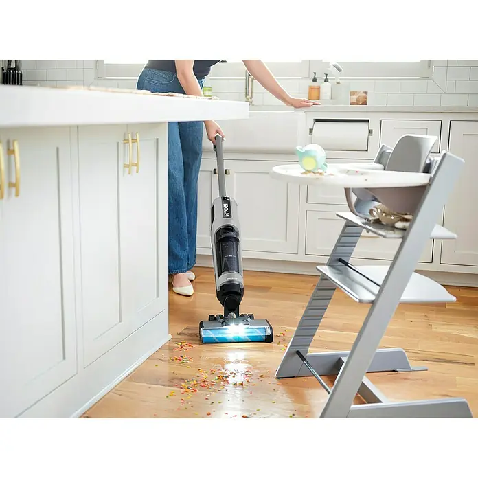Ryobi ONE+ Akku-Hartbodenreiniger RHFC18BL-0 - 18 V, Ohne Akku, Luftmenge: 710 l/min - Eine Person reinigt mit dem Ryobi Akku-Nass-/Trockensauger eine Küche mit Essensresten auf dem Boden. Das Gerät verfügt über eine blaue Bürste.
