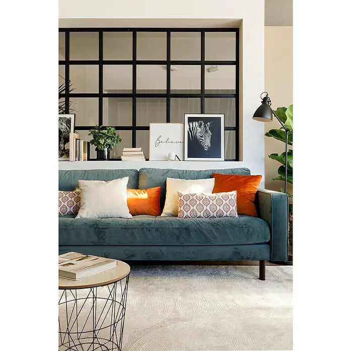 Cojín Pana - 45 x 45 cm, Poliéster, Crudo, Cuadrado - Acogedora sala de estar con un sofá verde azulado, cojines decorativos en diseños naranjas y estampados, una mesa redonda y elementos decorativos.