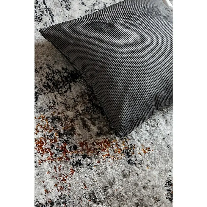Cojín Pana - 45 x 45 cm, Poliéster, Gris, Cuadrado - Primer plano de un cojín de pana gris sobre una alfombra con estampado abstracto. El cojín tiene una textura acanalada fina.