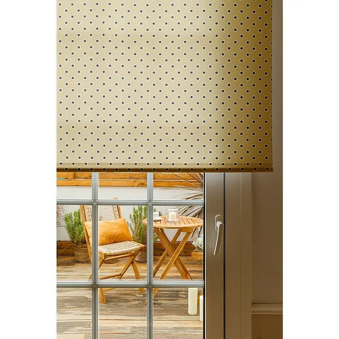 Cojín Velvet - 30 x 50 cm, Textil, Yema, Rectangular - Un estor enrollable amarillo de lunares cubre parcialmente una ventana con vista a muebles de jardín en un patio de madera.