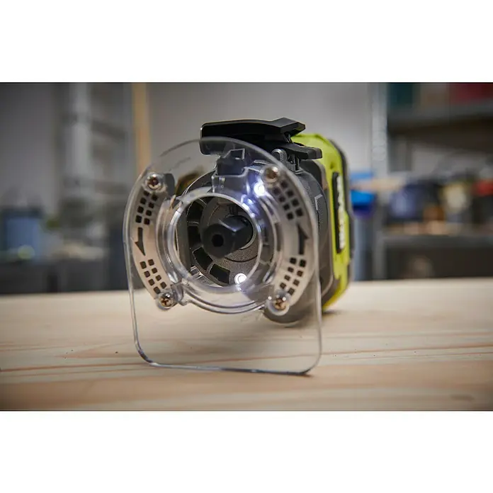 Ryobi ONE+HP Akku-Kantenfräser RTR18C-0 - 18 V, Ohne Akku - Nahaufnahme eines Ryobi-Kantenfräse mit transparenter Schutzvorrichtung auf einer Holzoberfläche, Fokus auf Präzision und Sicherheit.
