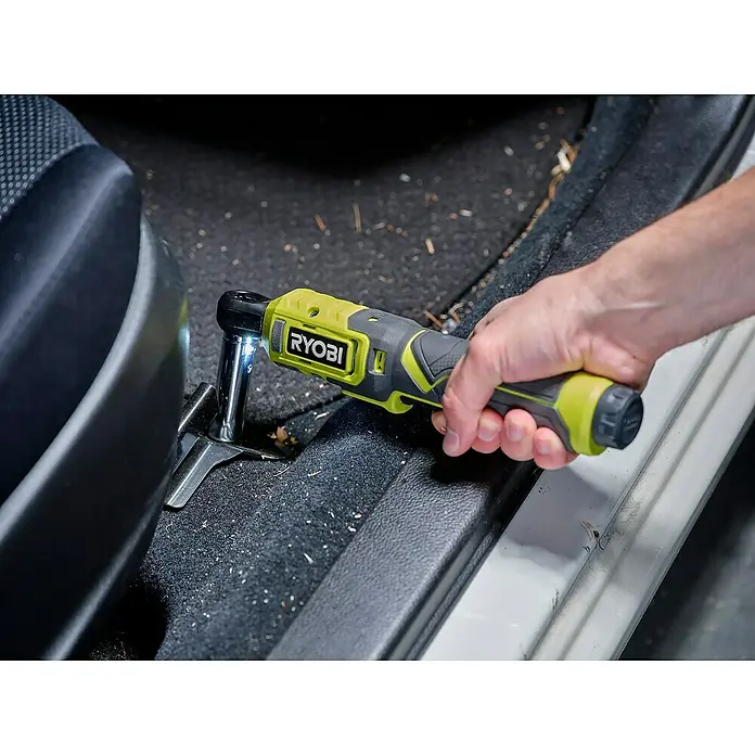 Ryobi 4V USB Akku-Ratschenschrauber RR14W4-0 - 4 V, Ohne Akku - Nahaufnahme eines RYOBI-Schlagschraubers, der an einem Sitz im Autoinnenraum befestigt wird, wobei der Fokus auf dem Werkzeug und seiner Verwendung liegt.