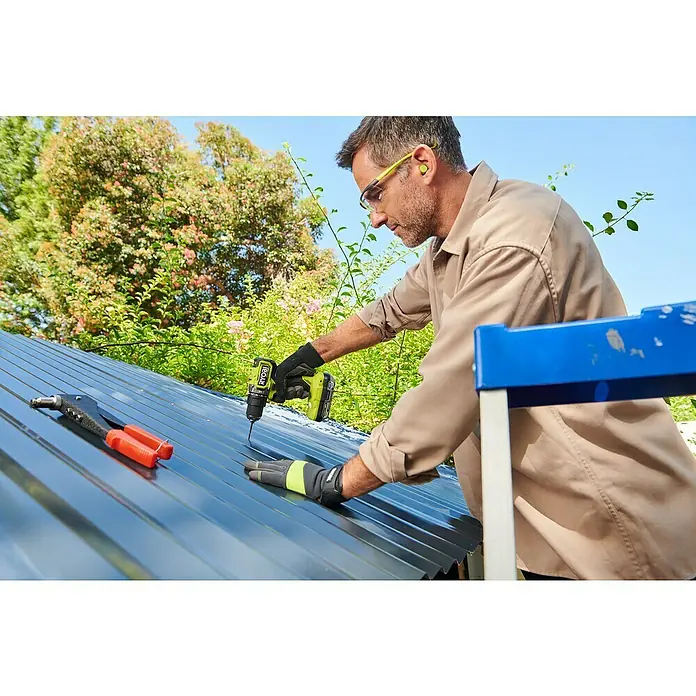 Ryobi ONE+ Akku-Schlagbohrschrauber RPD18C1-0 C - 18 V, Ohne Akku, 60 Nm - Ein Handwerker befestigt mit einem Ryobi-Bohrer eine Metallplatte auf einem Dach, wobei er Schutzbrille und Handschuhe trägt.