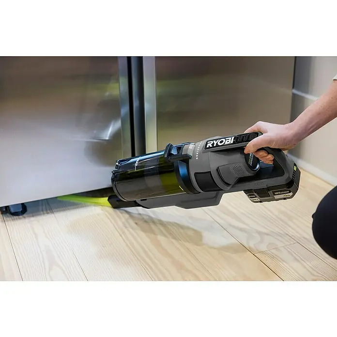 Ryobi ONE+ Akku-Staubsauger RSV18BL - 18 V, 1 Akku, 4 Ah, Behältervolumen: 0,8 l - Der Ryobi Akku-Staubsauger wird unter einem Kühlschrank benutzt, um den Boden zu reinigen. Der Staubsauger ist grau mit einem schwarzen Staubbehälter.