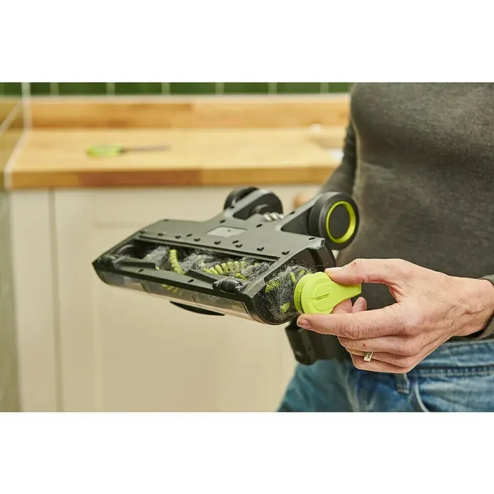 Ryobi ONE+ Akku-Staubsauger RSV18BL - 18 V, 1 Akku, 4 Ah, Behältervolumen: 0,8 l - Eine Person reinigt die Bürste eines Staubsaugers mit einem grünen Reinigungswerkzeug. Die Bürste ist mit Haaren und Staub verstopft.