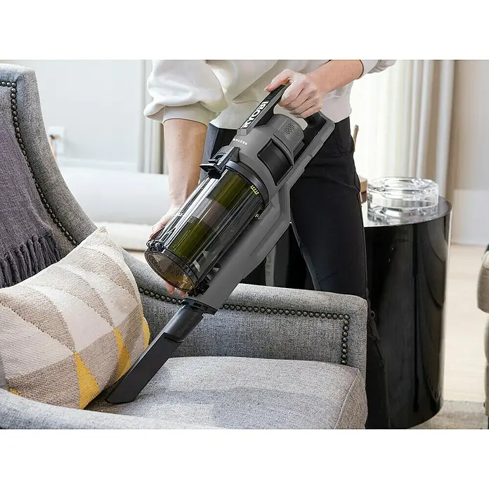 Ryobi ONE+ Akku-Staubsauger RSV18BL - 18 V, 1 Akku, 4 Ah, Behältervolumen: 0,8 l - Eine Person benutzt einen Ryobi Akku-Staubsauger zur Reinigung eines Sessels. Der Staubsauger ist grau mit einem durchsichtigen Behälter.