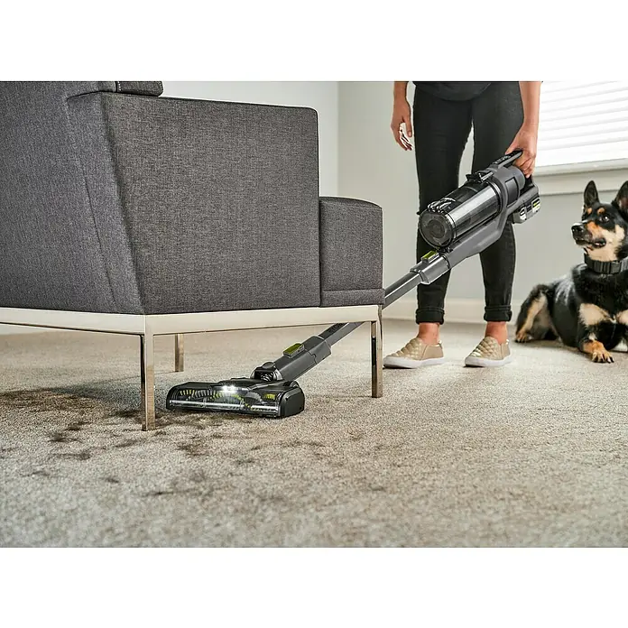 Ryobi ONE+ Akku-Staubsauger RSV18BL - 18 V, 1 Akku, 4 Ah, Behältervolumen: 0,8 l - Eine Person benutzt einen RYOBI Akku-Staubsauger, um unter einem Sofa zu saugen, während ein Hund zusieht.