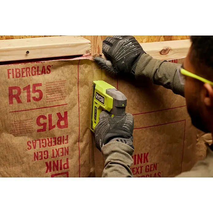 Ryobi 4V USB Akku-Tacker RST4-0 - 4 V, Ohne Akku - Nahaufnahme eines Ryobi-Elektrotackers, der zum Anbringen von Glasfaserisolierung an einer Wand verwendet wird. Werkzeug für Heimwerkerprojekte.