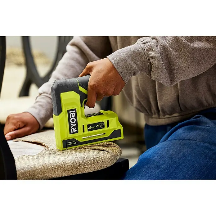 Ryobi 4V USB Akku-Tacker RST4-0 - 4 V, Ohne Akku - Nahaufnahme eines Ryobi 4-in-1-Elektrotackers beim Befestigen von Stoff an einem Möbelstück, der Komfort und Vielseitigkeit bietet.