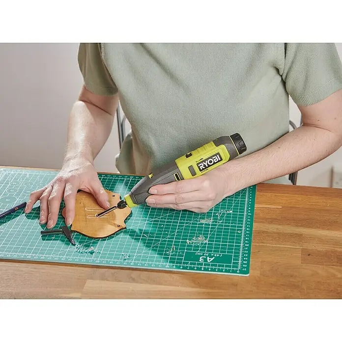Ryobi 4V USB Akku-Schnitzer RPC4-0 - 4 V, Ohne Akku - Nahaufnahme eines Ryobi-Rotationswerkzeugs in Aktion, das zum Gravieren eines Holzstücks auf einer Schneidematte verwendet wird.