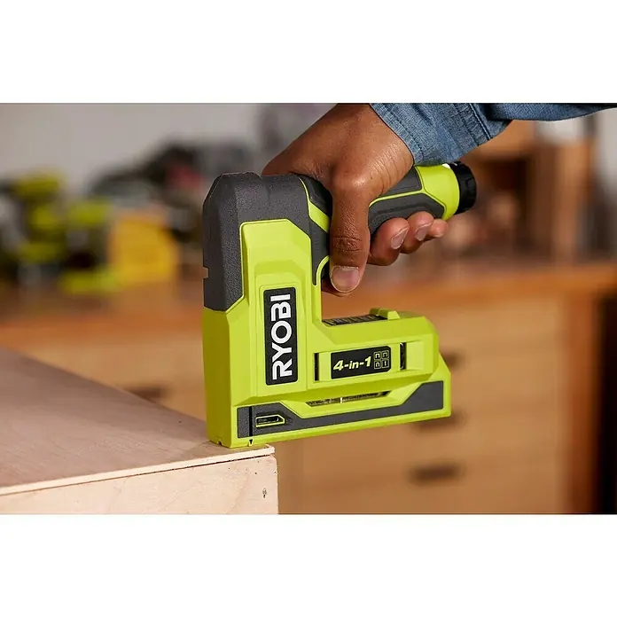 Ryobi 4V USB Akku-Tacker RST4-0 - 4 V, Ohne Akku - Ein gelber Ryobi 4-in-1-Elektrotacker wird von einer Hand über einem Holzstück gehalten. Das Werkzeug ist bereit zum Heften.