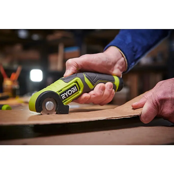Ryobi 4V USB Akku-Universalschere RCT4-0 - 4 V, Ohne Akku - Nahaufnahme eines Ryobi-Rotationsschneiders, der von einer Hand gehalten wird, während er durch ein Stück Karton schneidet.
