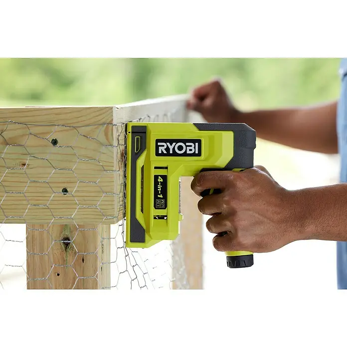 Ryobi 4V USB Akku-Tacker RST4-0 - 4 V, Ohne Akku - Eine Nahaufnahme eines RYOBI 4-in-1-Tackers, der an einem Holzzaun mit Drahtgeflecht befestigt wird.