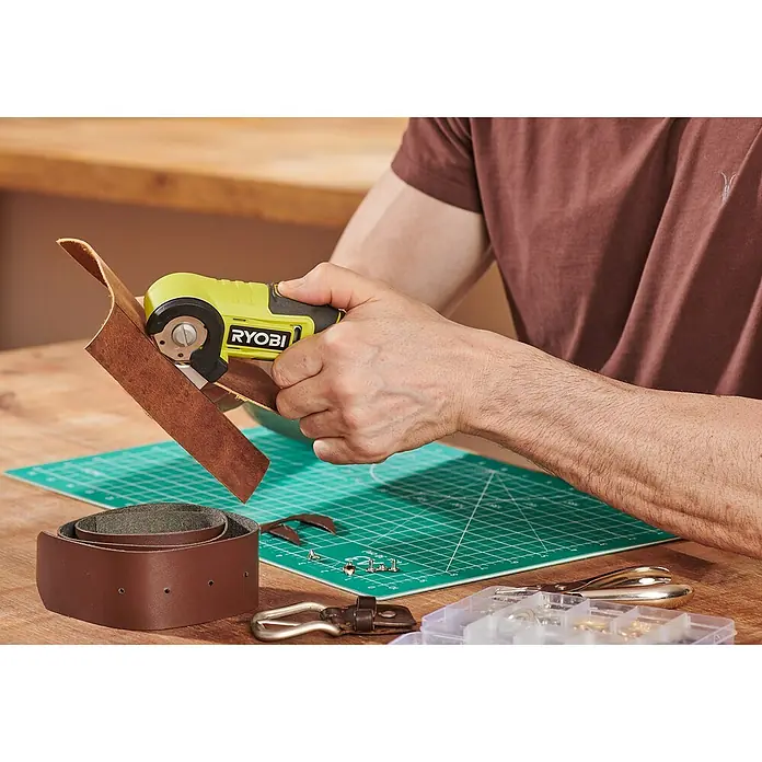 Ryobi 4V USB Akku-Universalschere RCT4-0 - 4 V, Ohne Akku - Nahaufnahme eines Mannes, der mit einem RYOBI-Rotationsschneider ein Lederstück bearbeitet, ideal für Bastelprojekte und Lederarbeiten.
