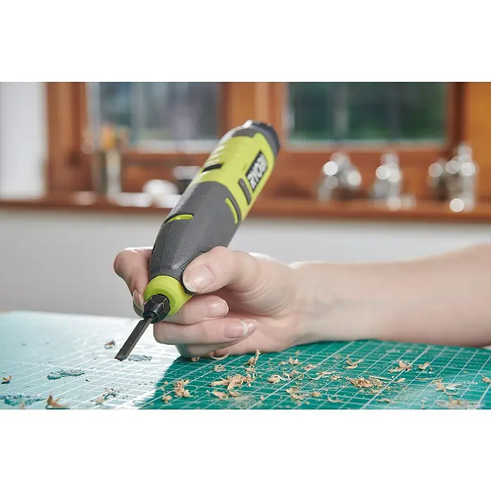Ryobi 4V USB Akku-Schnitzer RPC4-0 - 4 V, Ohne Akku - Nahaufnahme eines Ryobi-Elektrowerkzeugs in Aktion, das Holz bearbeitet und Späne auf einer grünen Matte hinterlässt.