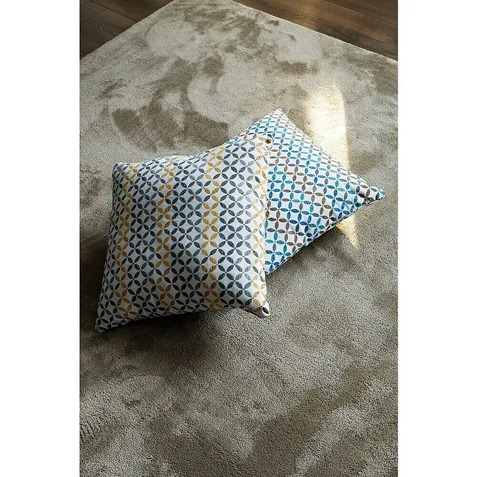 Cojín Yunus - 45 x 45 cm, Textil, Mostaza, Cuadrado - Dos cojines decorativos con diseños geométricos sobre una alfombra beige. Los cojines presentan un diseño amarillo-gris y azul-marrón.