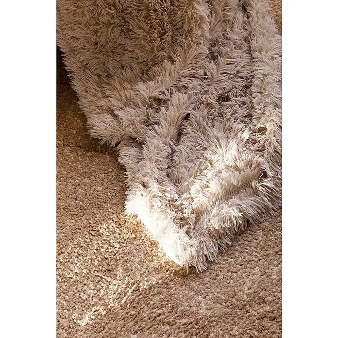 Manta para sofá New Luxury - 160 x 220 cm, Poliéster, Beige - Primer plano de una manta beige y peluda que descansa sobre una alfombra de color similar, resaltada por luz suave.