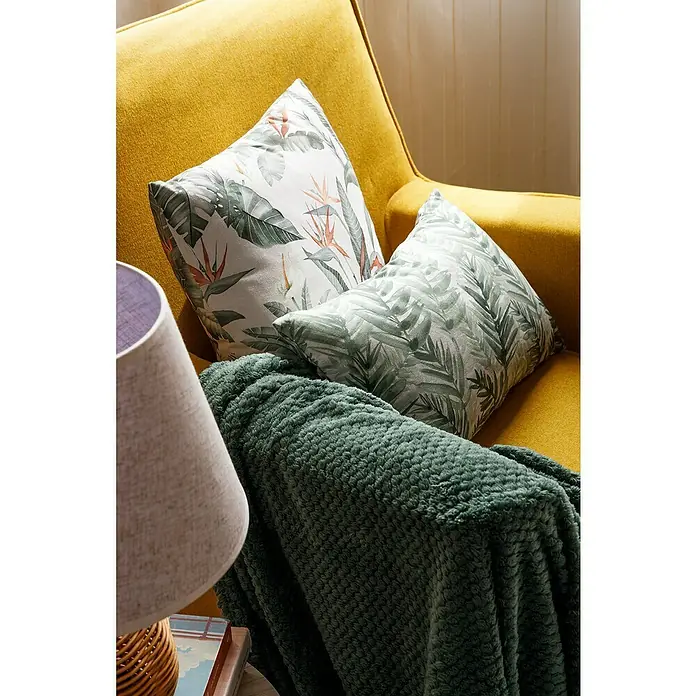 Manta para sofá Stelvio - 160 x 220 cm, Poliéster, Kaki - Primer plano de un sillón amarillo adornado con cojines con estampados de plantas y una manta verde.