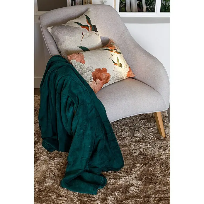 Manta para sofá Pirineos - 130 x 150 cm, Poliéster, Surtido - Cómoda butaca con cojines y una manta verde sobre una alfombra, creando un ambiente acogedor.