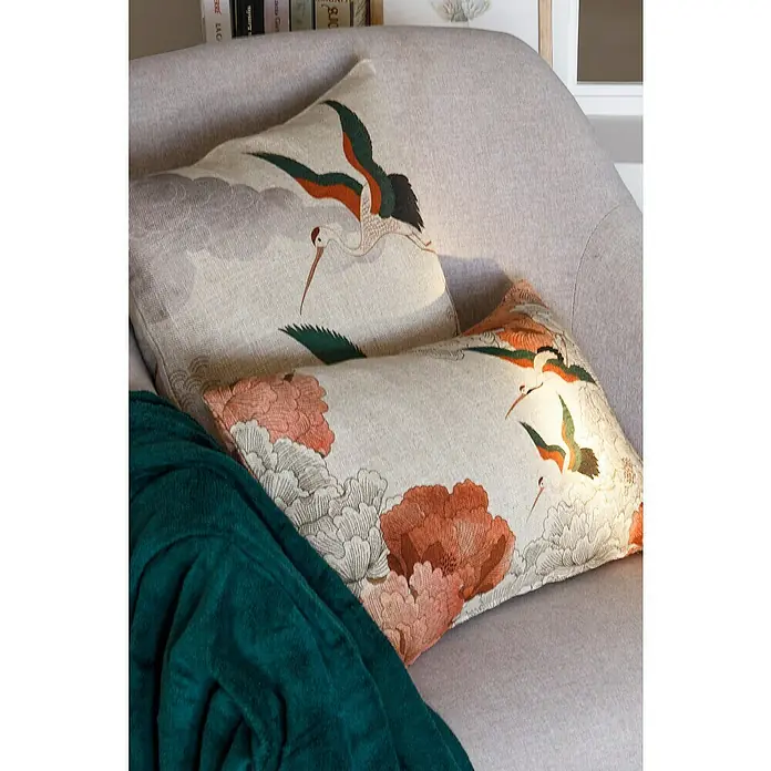 Manta para sofá Pirineos - 130 x 150 cm, Poliéster, Surtido - Dos cojines decorativos con diseños florales y de grulla descansando sobre un sofá, complementados con una manta verde.