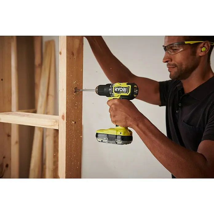 Ryobi ONE+HP Akku-Bohrschrauber RDD18C1-0 C - 18 V, Ohne Akku, 60 Nm - Ein Mann benutzt einen Ryobi ONE+ HP Akku-Bohrschrauber, um ein Holzstück zu befestigen, mit Schutzbrille und Gehörschutz für Sicherheit.