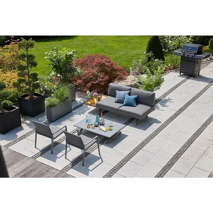 Sunfun Loungemöbel-Set Lumar - 5 -tlg., Aluminium, Teak, Ablagefläche rechts, Night-Grey - Eine Gartenszene mit grauen Gartenmöbeln, darunter ein Sofa, Stühle und ein Tisch, umgeben von üppigem Grün und einem Grill im Hintergrund.